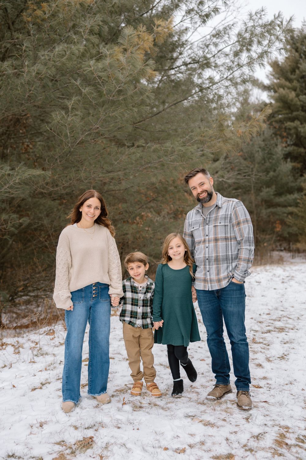 A family portrait session on a snow-covered hill with pine trees in winter.