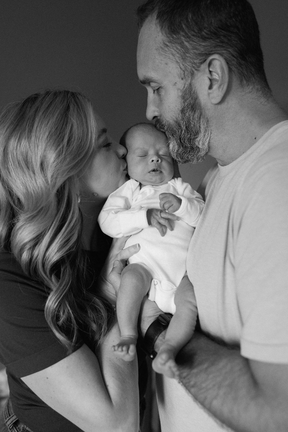 An intimate black and white portrait of a family sharing a tender moment with their newborn baby.