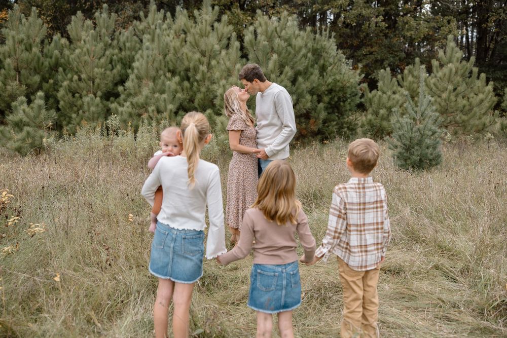 A candid family moment captured in a field with evergreen trees in the background.