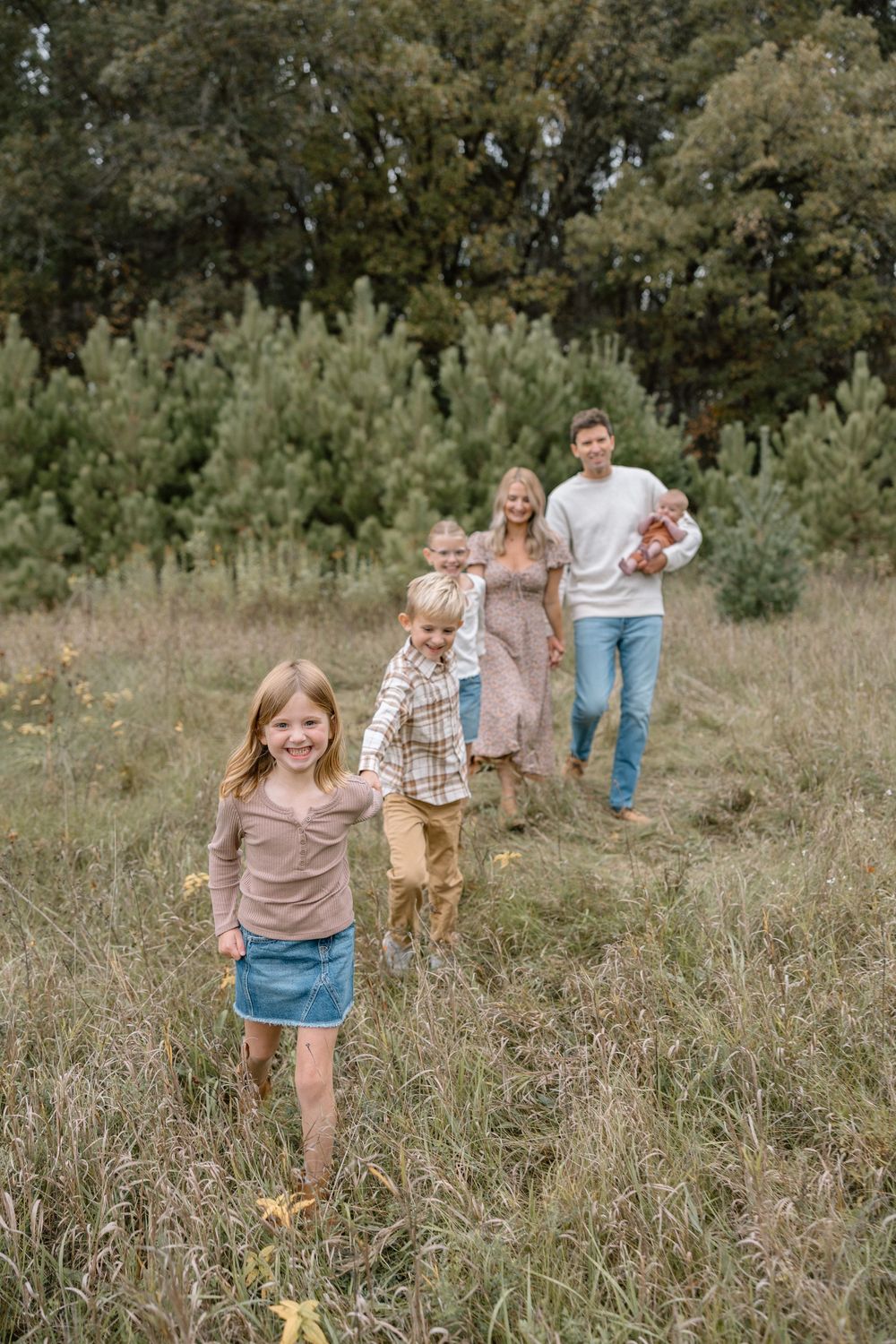 A playful family scene with children running through a grassy field while parents follow behind.