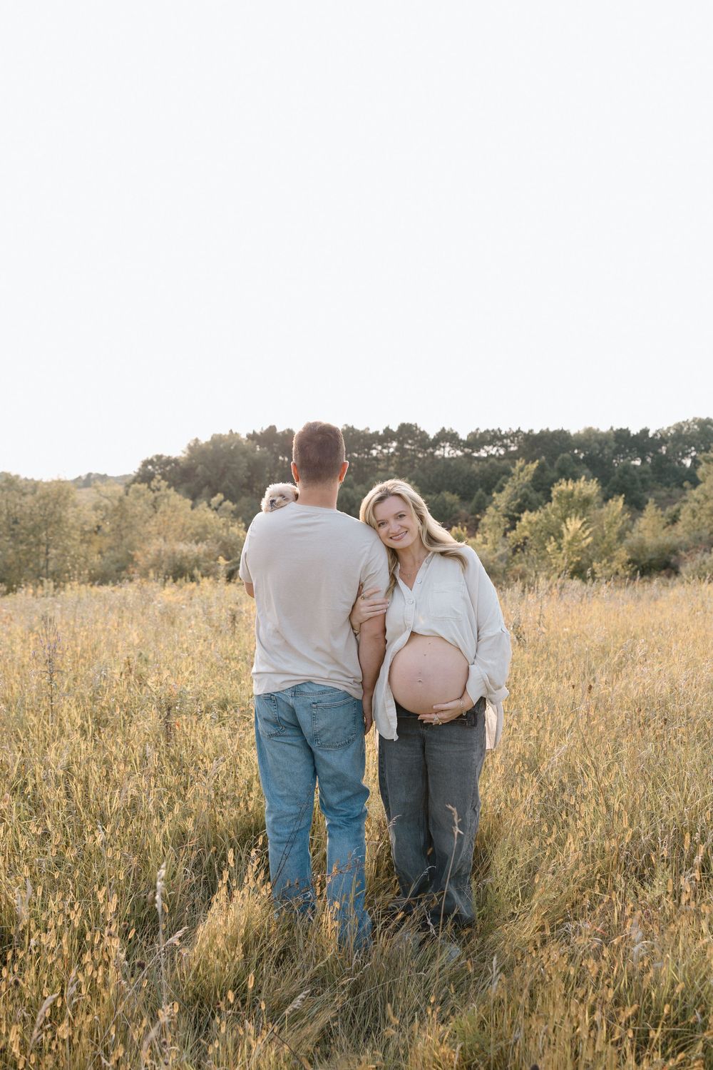Two people walk hand in hand through a tall grass meadow at golden hour.