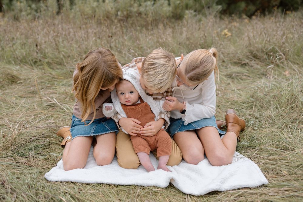 Children sitting together on a white blanket in a grassy field sharing a sweet moment.