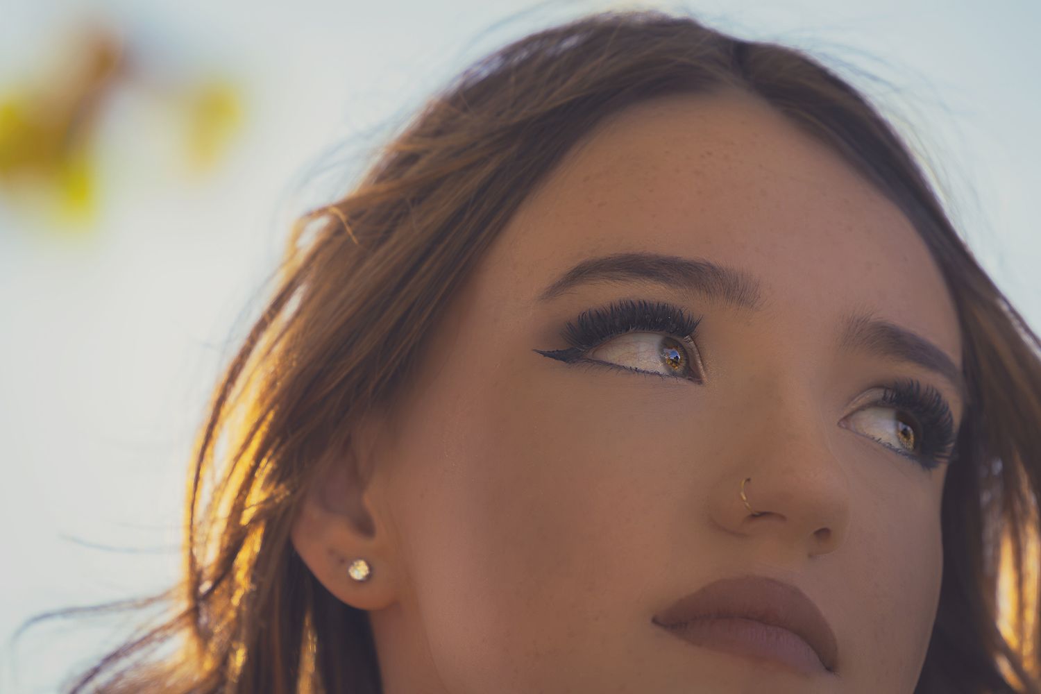 Close up portrait with brown lipstick and pearl earrings during golden hour lighting.
