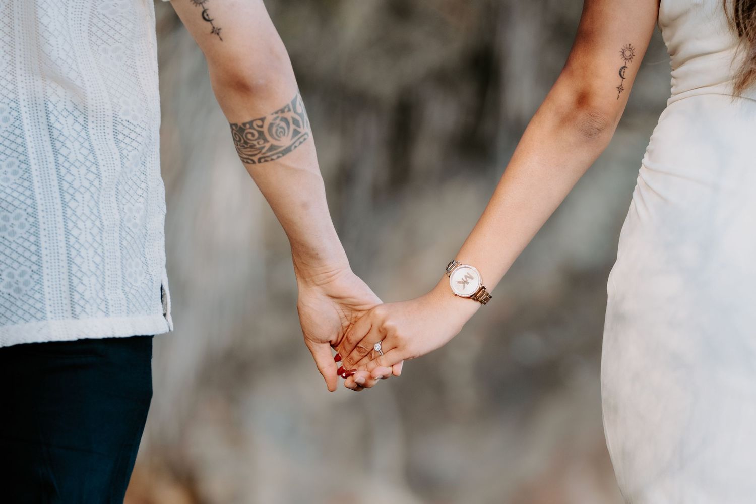 A close-up shot of two people holding hands, showing a tattoo and watch details.