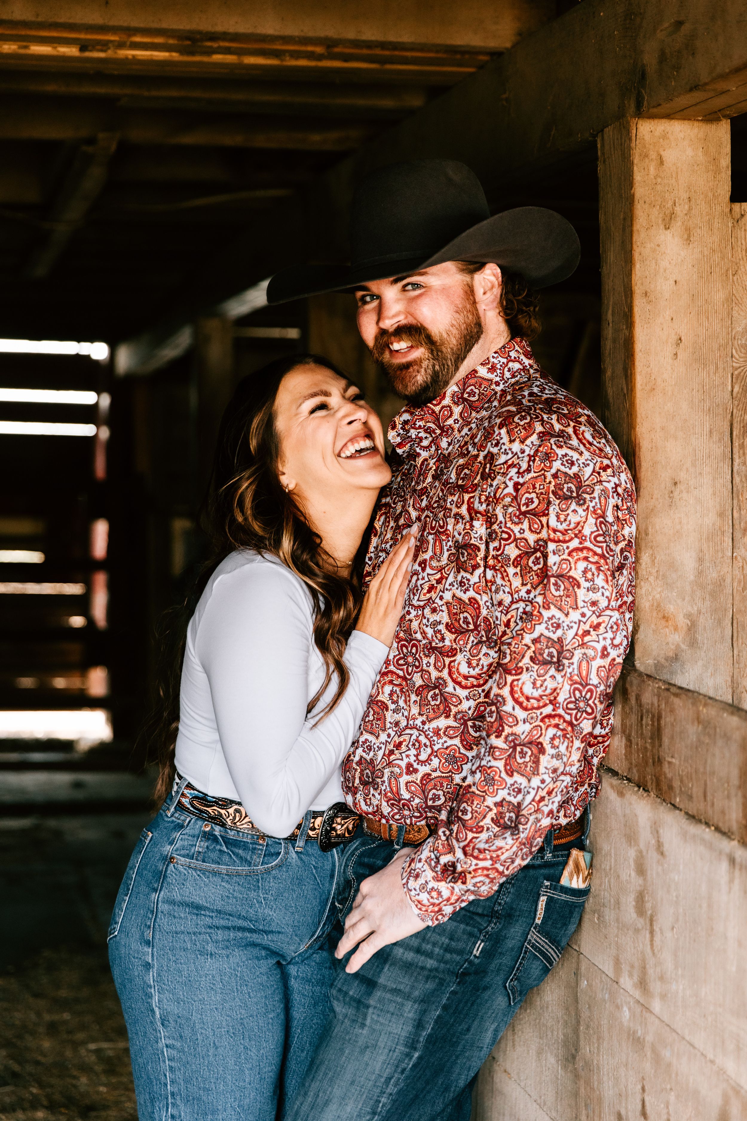 A couple pose in the family ranch horse barn in Hosper, Iowa for their engagement photos.