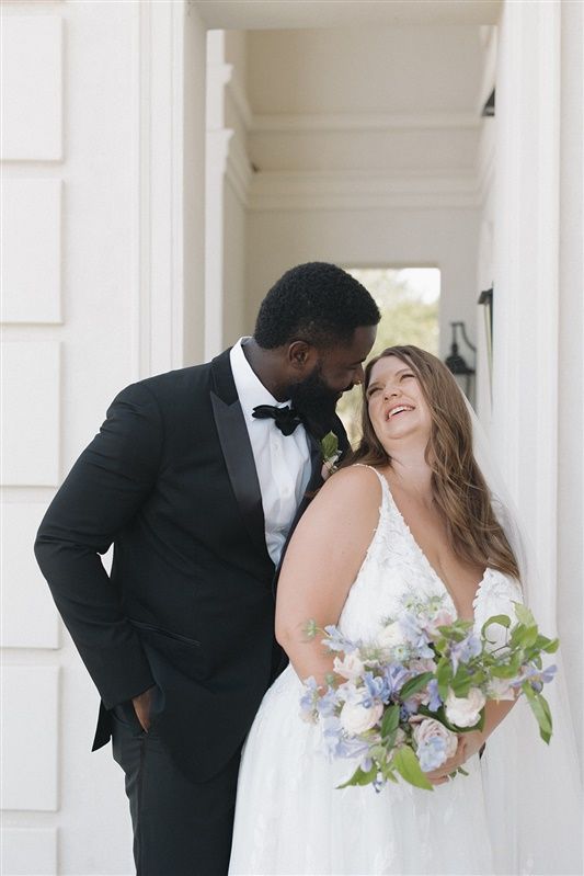 A lovely wedding couple shares a joyful moment together on their special day, with the bride holding a purple bouquet.
