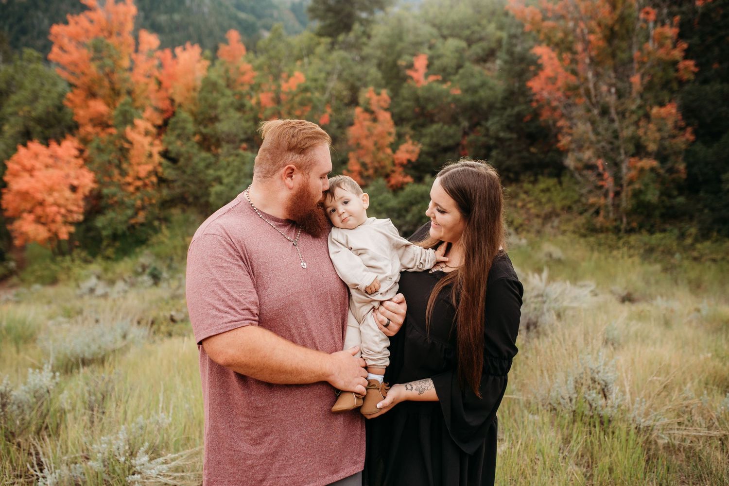 Family portrait in an outdoor setting with fall colors and mountain scenery in the background.