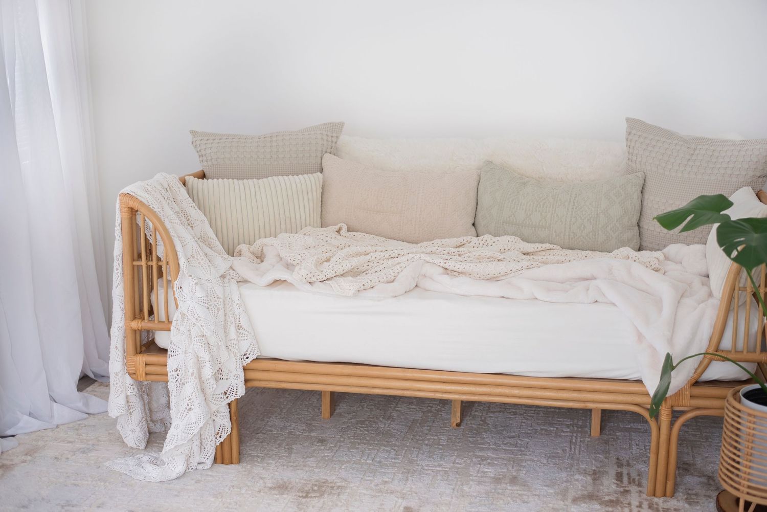 Cozy rattan daybed with neutral beige cushions and pillows arranged against a white wall with minimal decor.