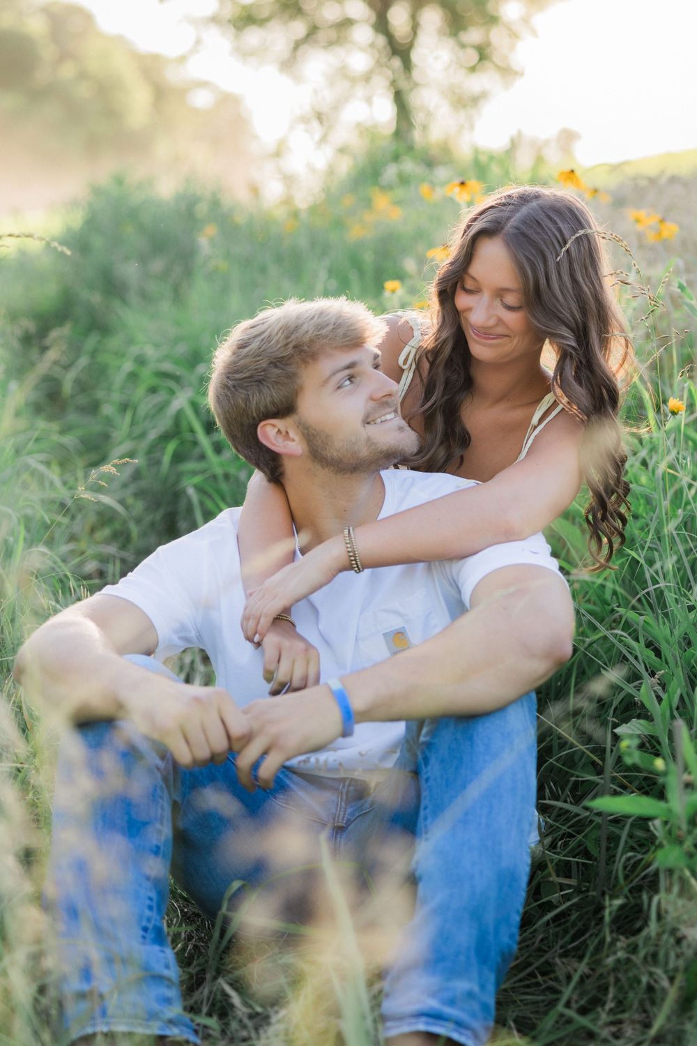 Romantic couple embracing in a wildflower field during golden hour sunset.