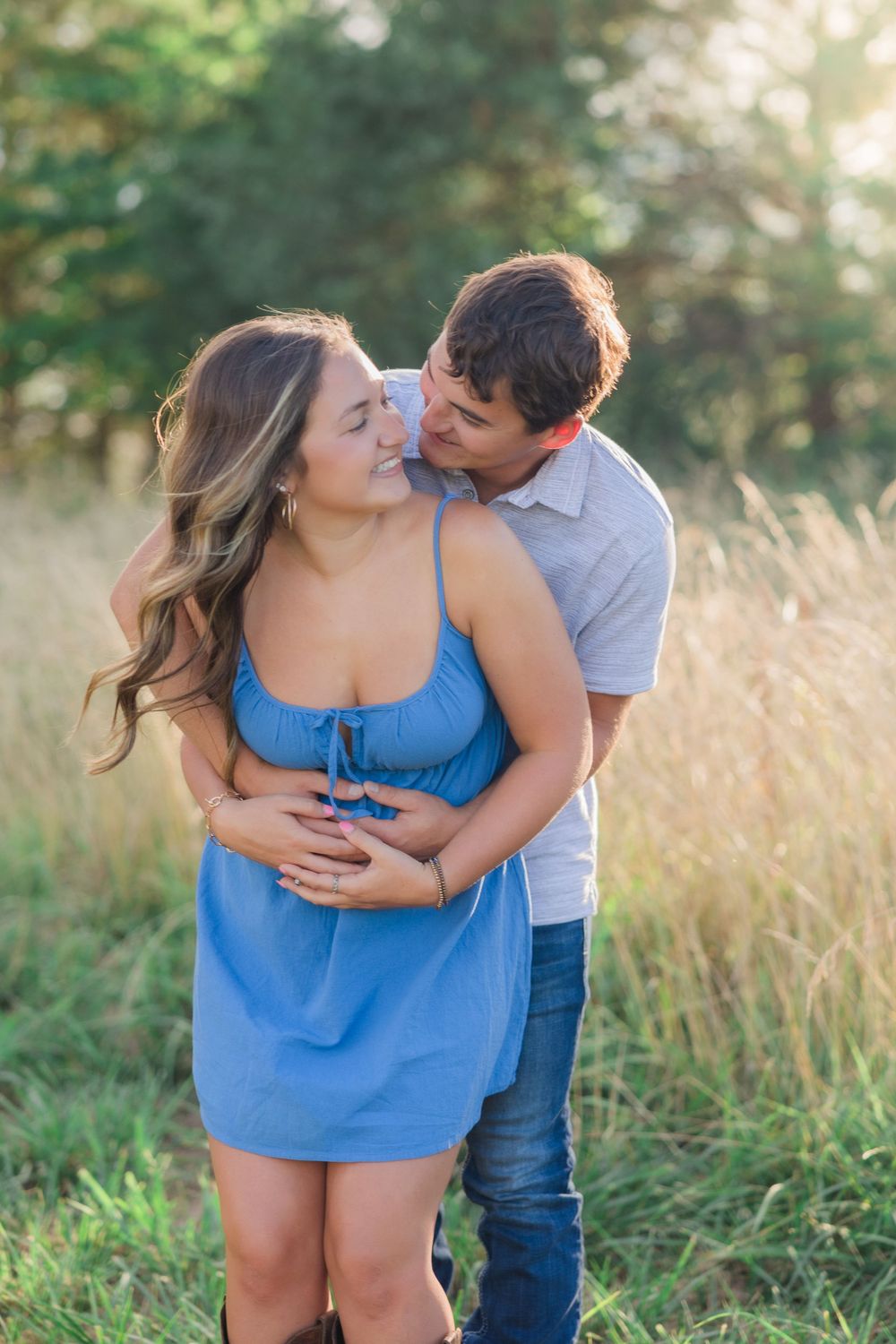 Couple embracing in summer field wearing blue dress and grey polo.