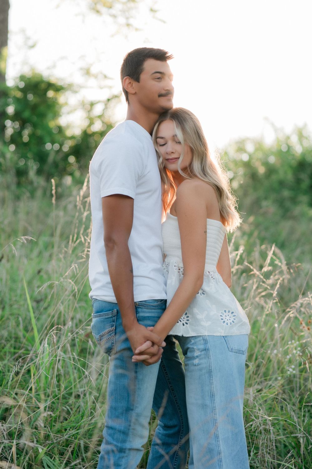 Joyful couple holding hands and laughing together in tall grass field.