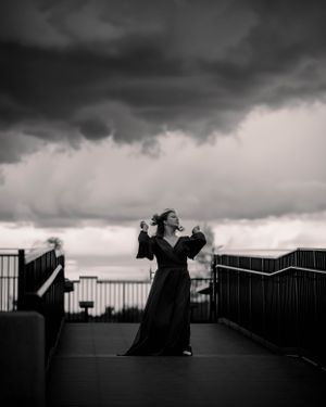 Silhouette of a person in a flowing black dress stands on a balcony against dramatic stormy clouds in black and white portrait in Abilene TX