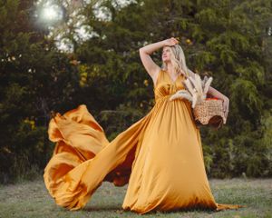 A person in a flowing mustard yellow maxi dress poses in a field with a basket during golden hour portrait by Higher RES Visuals in Abilene