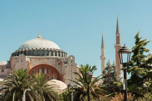 View of Hagia Sophia's iconic dome and minarets with palm trees and a vintage lamp post in Istanbul, Turkey travel photography