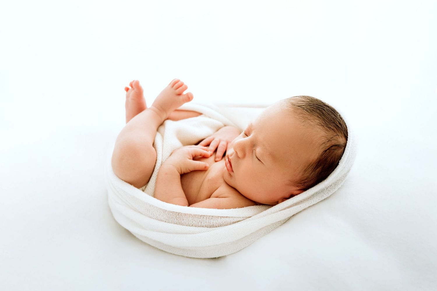 Sleeping newborn baby wrapped in white blanket on light background.