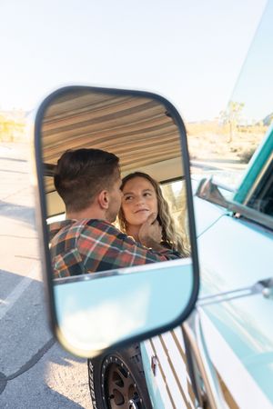 A romantic moment captured through a car side mirror shows a couple in a vintage vehicle during sunset.