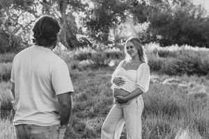 A soon to be mom standing in a grassy field in North Carolina while holding her belly and looking at her husband
