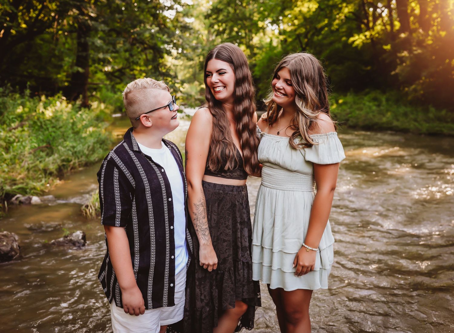 Three people laughing together outdoors on a wooded path during sunset.