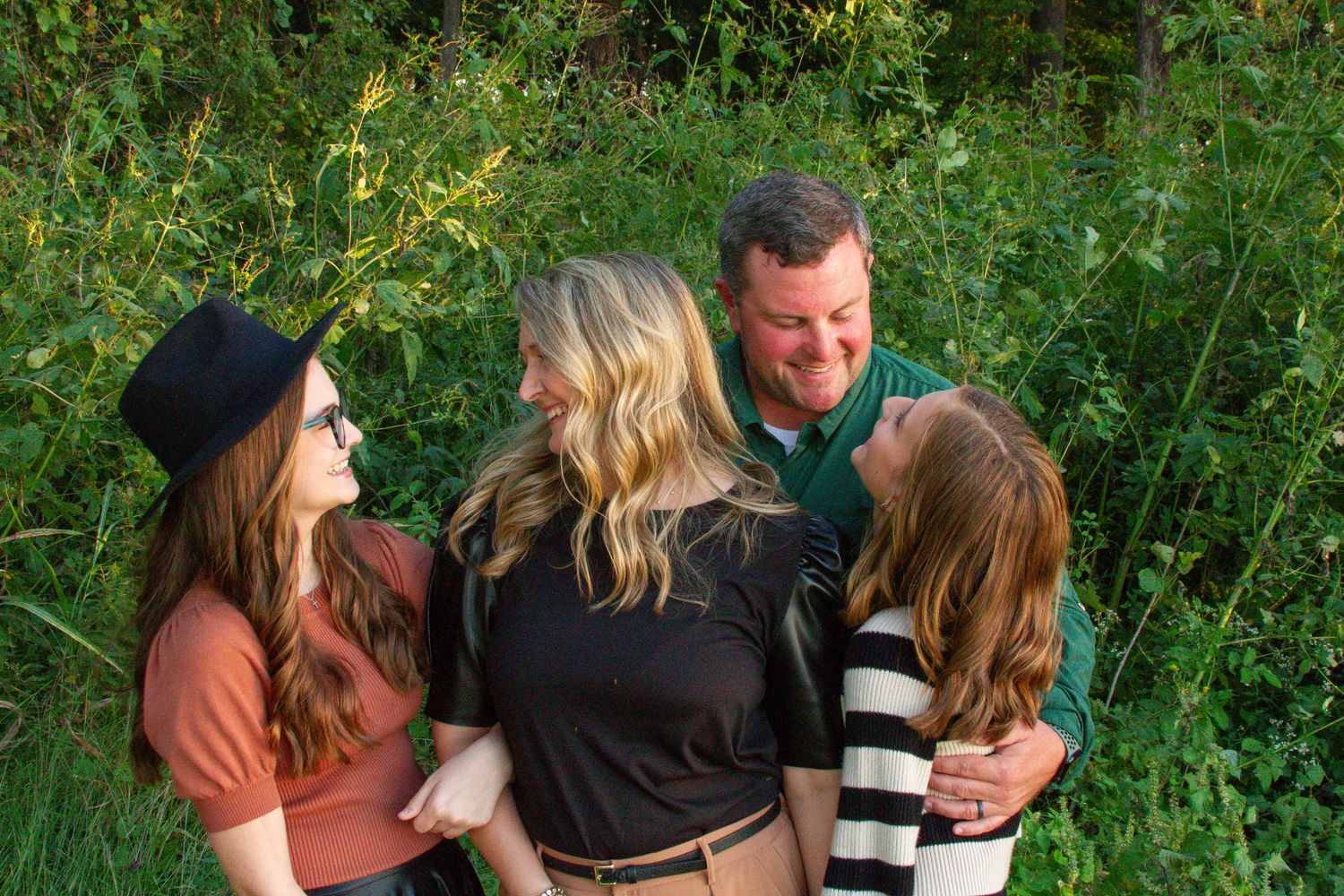 a family of four, mom, dad, and two preteen daughters in a grassy area