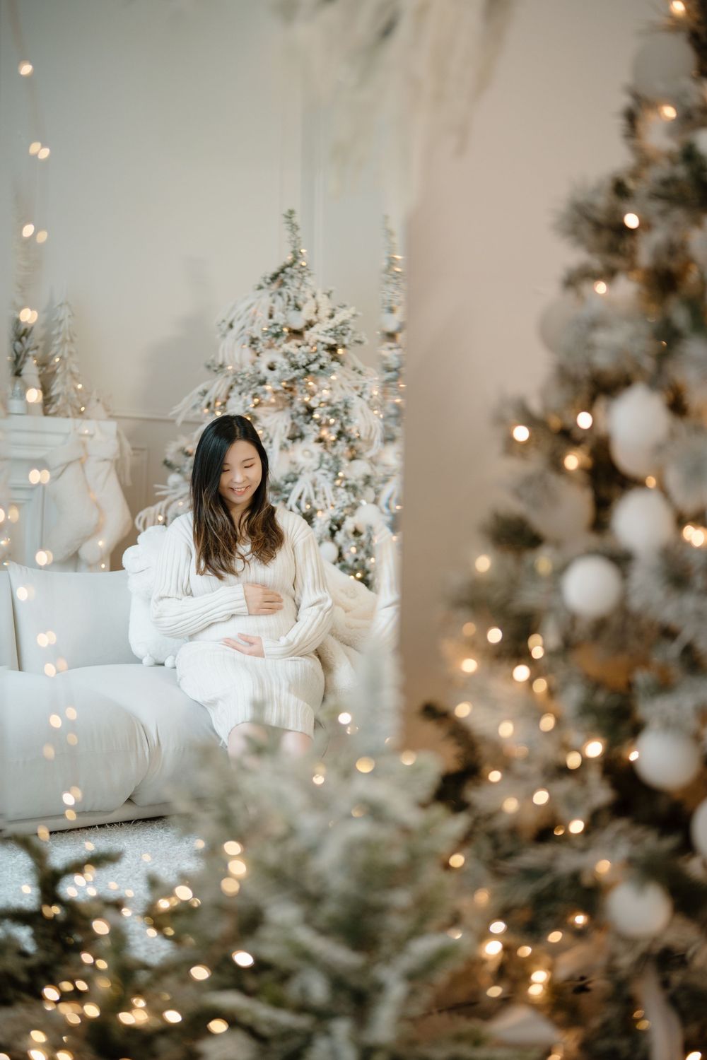 Cozy Christmas scene with white and gold decorations, twinkling lights, and figures sitting by a decorated tree.
