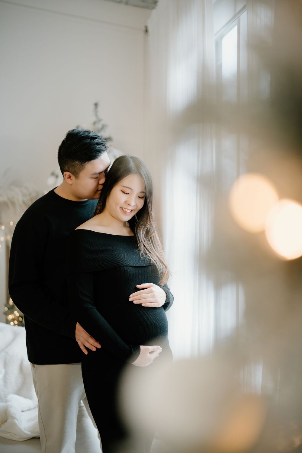 A romantic couple embraces intimately in a bright white room with soft window lighting casting dreamy shadows.