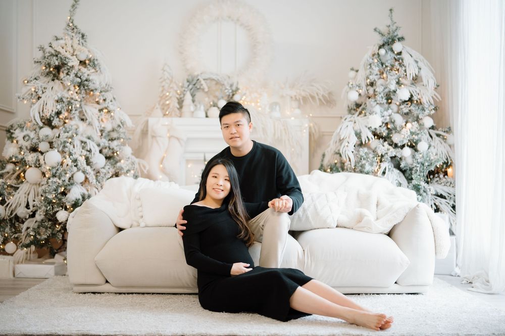 A couple lounges on white furniture in a bright modern room decorated with snowy Christmas trees.