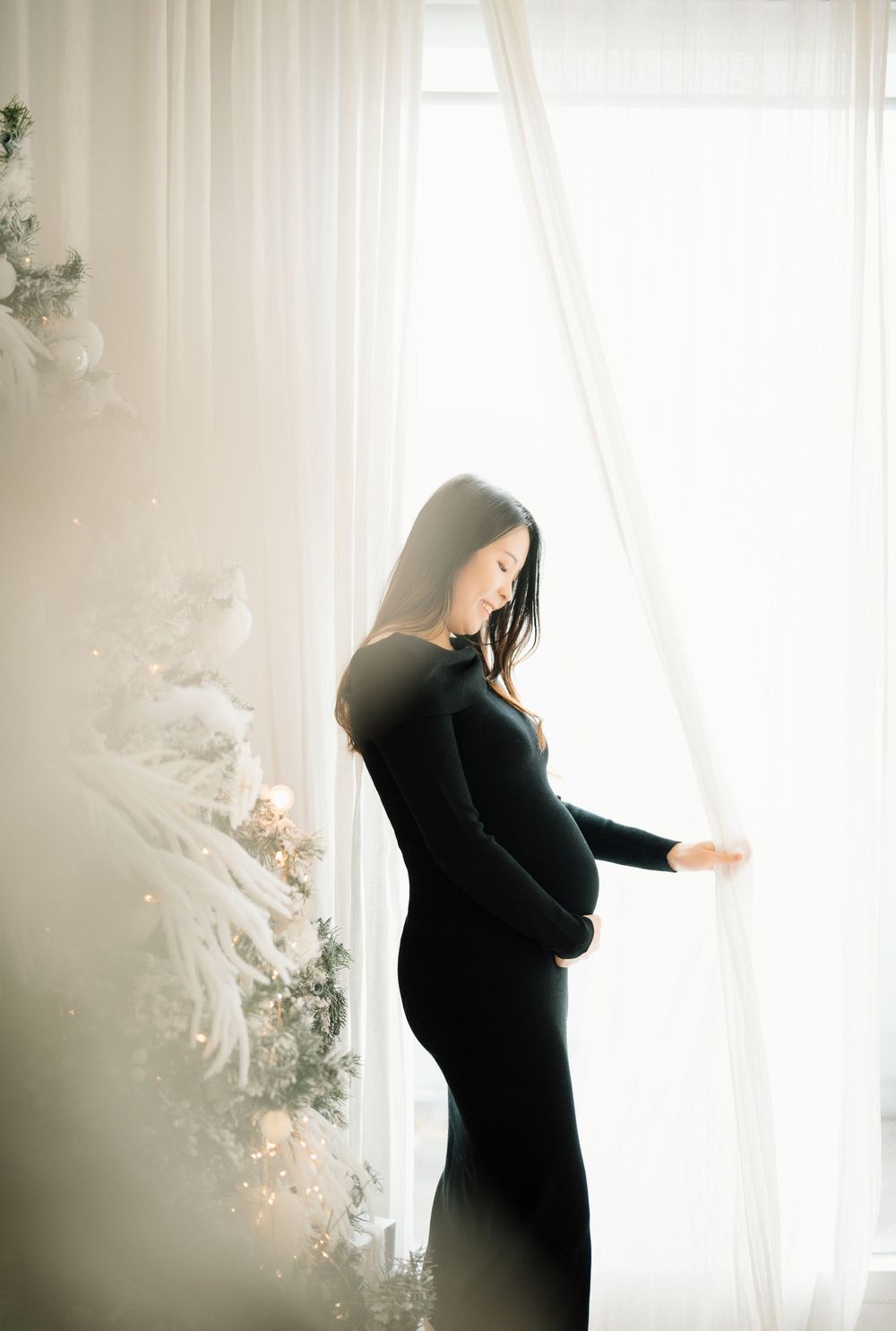 A silhouetted figure stands against bright window light in an ethereal winter scene with white decor.