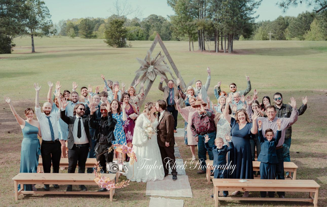 Whole group wedding photo after ceremony in shaded field at Sanctuaire Atelier.