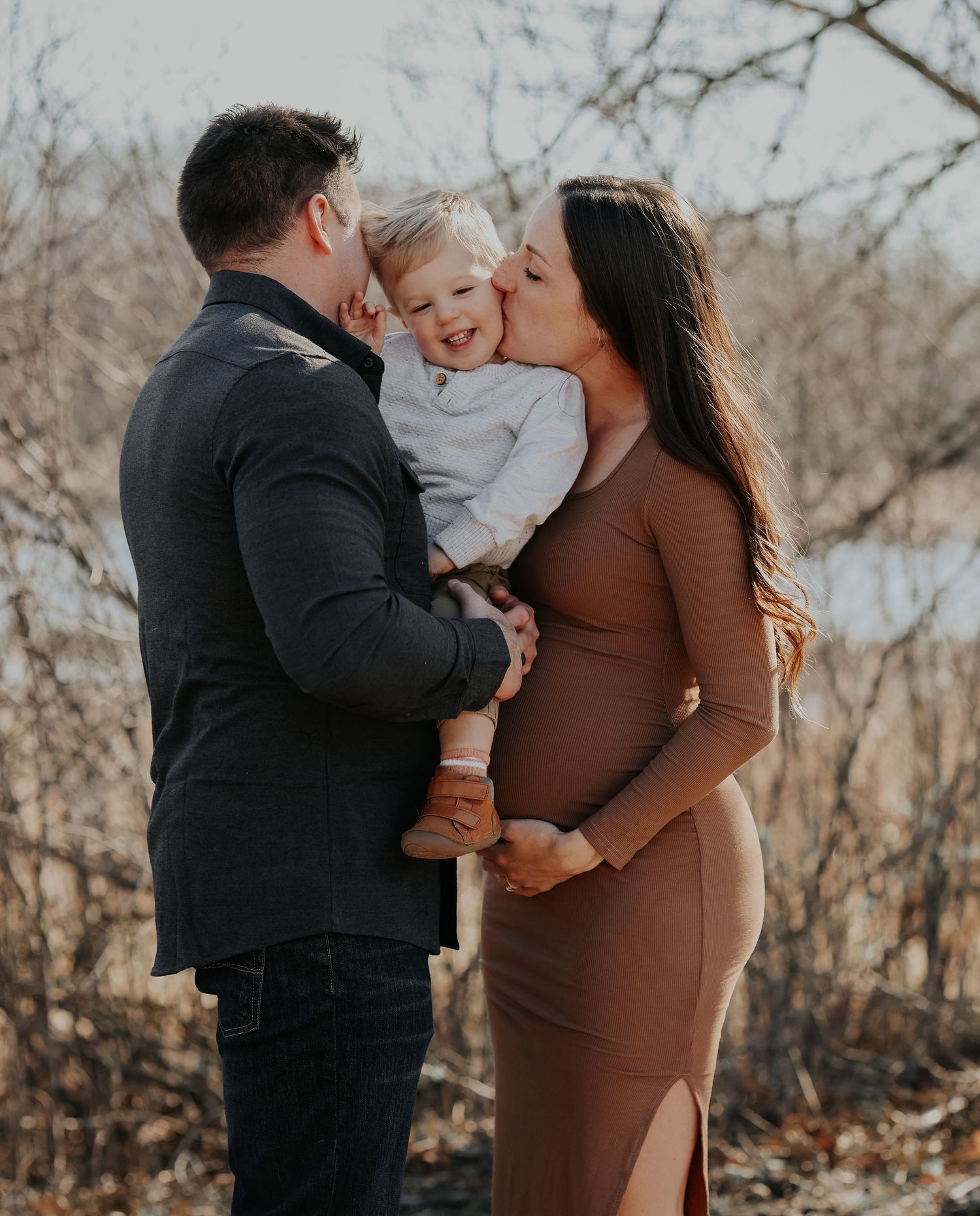 A loving family shares kisses with their toddler during a winter maternity photoshoot.