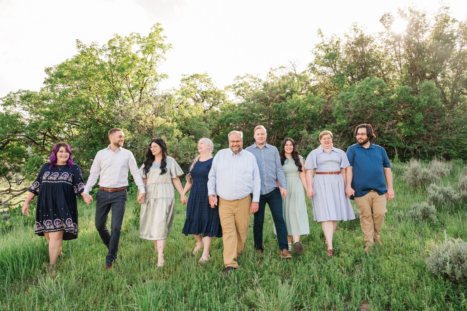 A group portrait of people standing together in casual attire on a grassy hillside during golden hour.