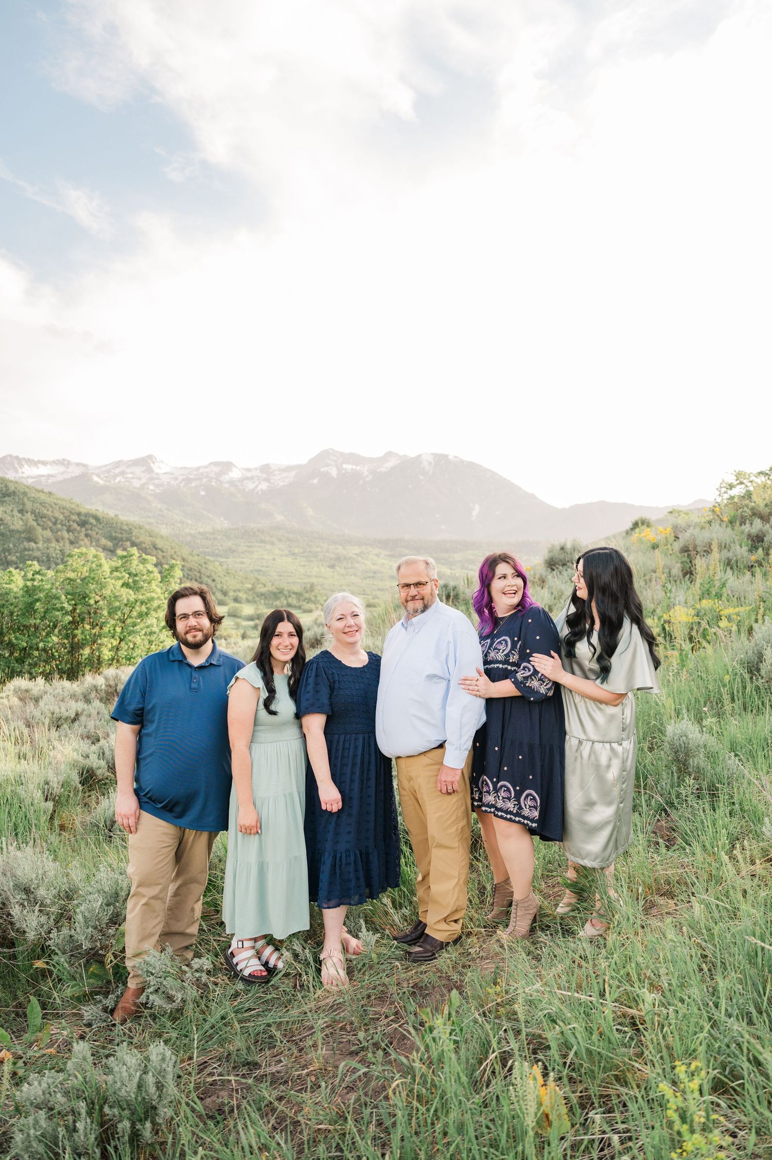 Casual outdoor family photo session with mountains and bright sky in the background.