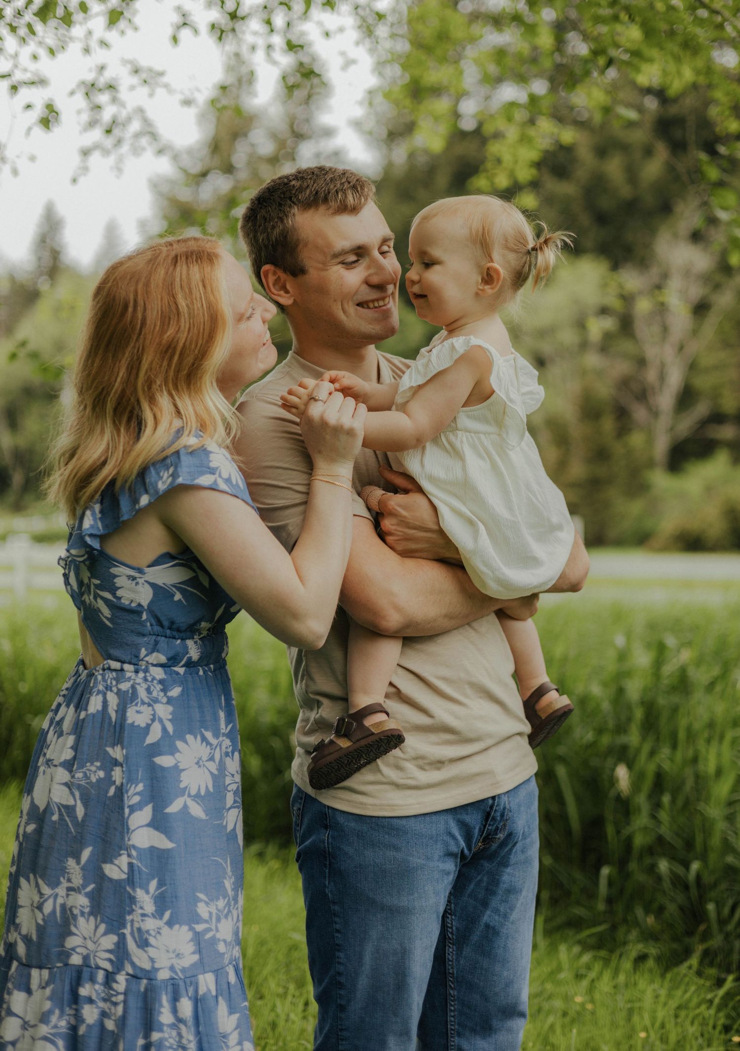 Family of three posing outdoors, parents smiling at toddler in father's arms.