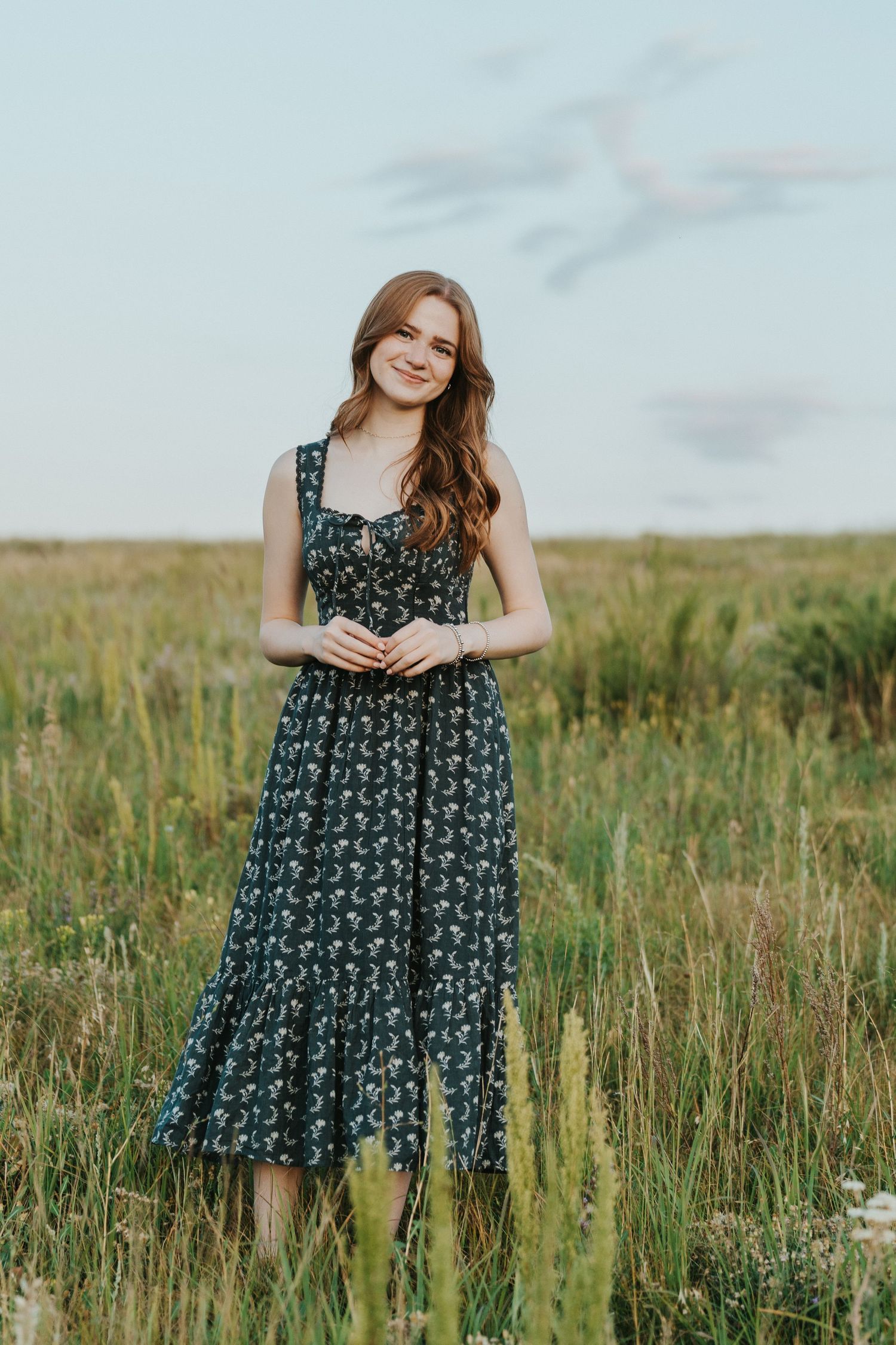 Senior girl stands in a green grassy field with blue sky