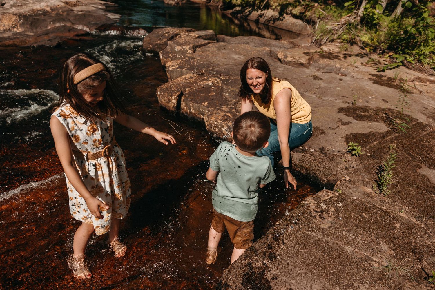 A woman and two children playing in a shallow rocky stream surrounded by lush greenery on a sunny day. Whitney Popp, Phoenix AZ photographer