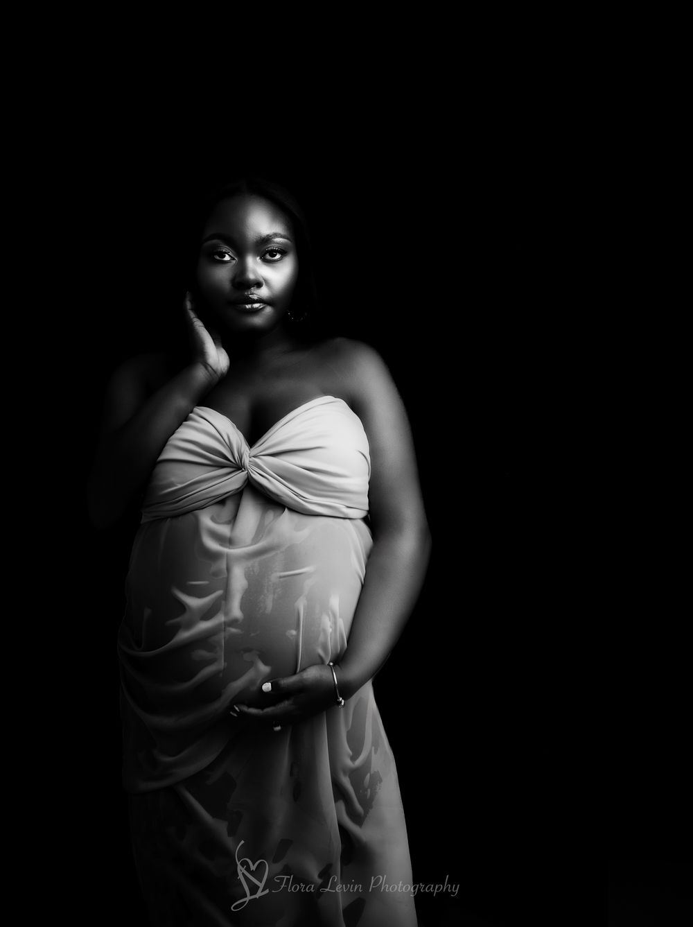 Fine Art black and white portrait  showing pregnant woman in white wet top against dark background with moody lighting.