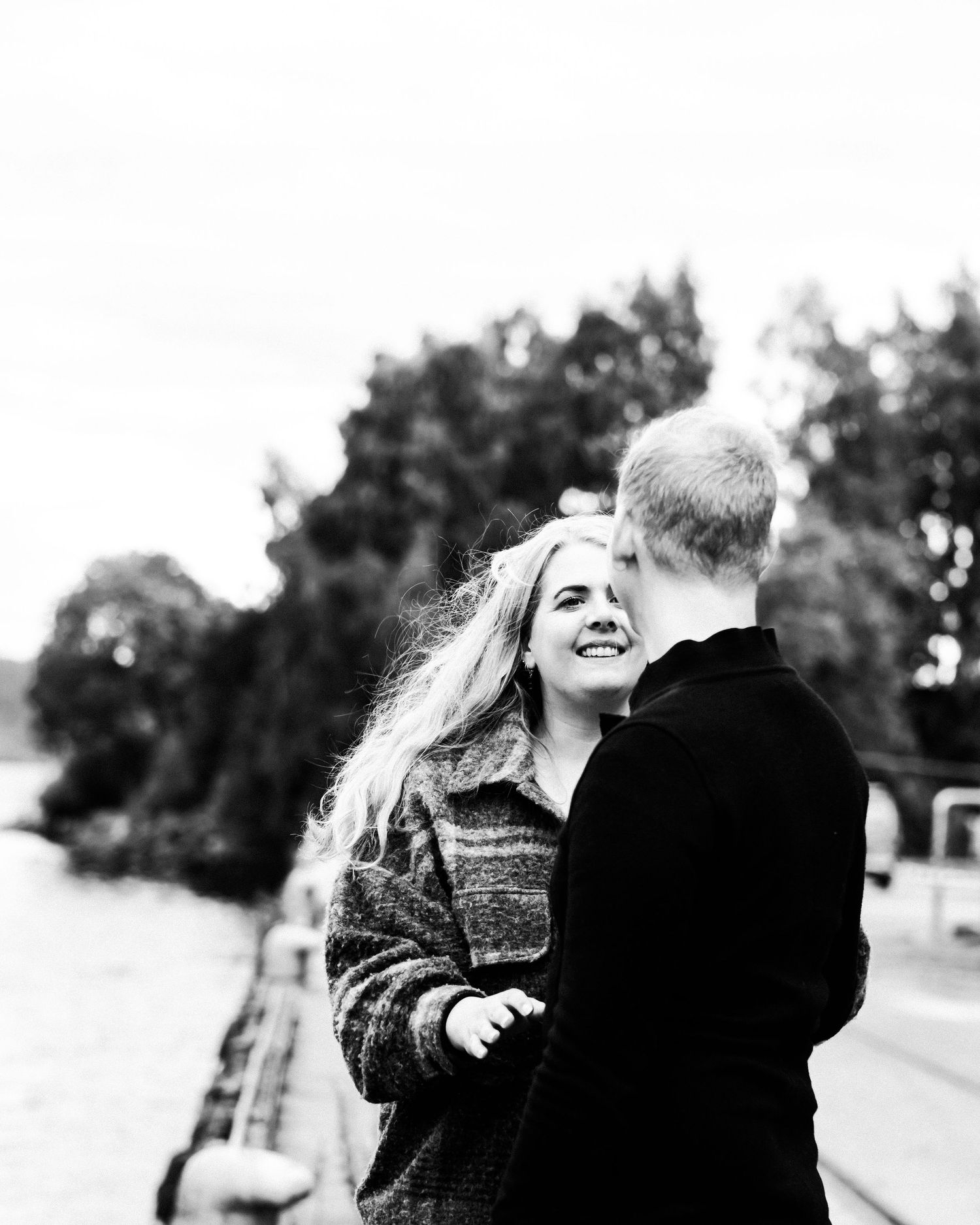 Romantic couple sharing a laugh on a bridge in black and white photography.