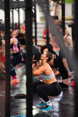 Woman doing a wall ball squat exercise in a CrossFit gym during a group fitness class.