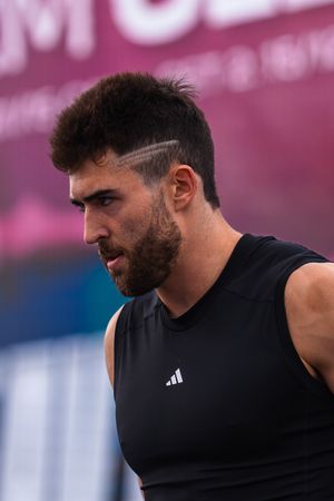 Muscular man with stylish haircut wearing black Adidas sleeveless shirt at outdoor sports event.