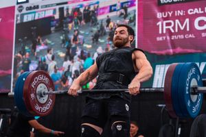 Male athlete performs a heavy deadlift at a CrossFit competition with Rogue barbells on a stadium stage.
