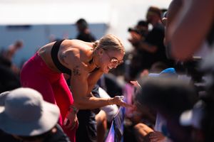 Female CrossFit athlete in pink leaning over barrier interacting with crowd at outdoor competition.