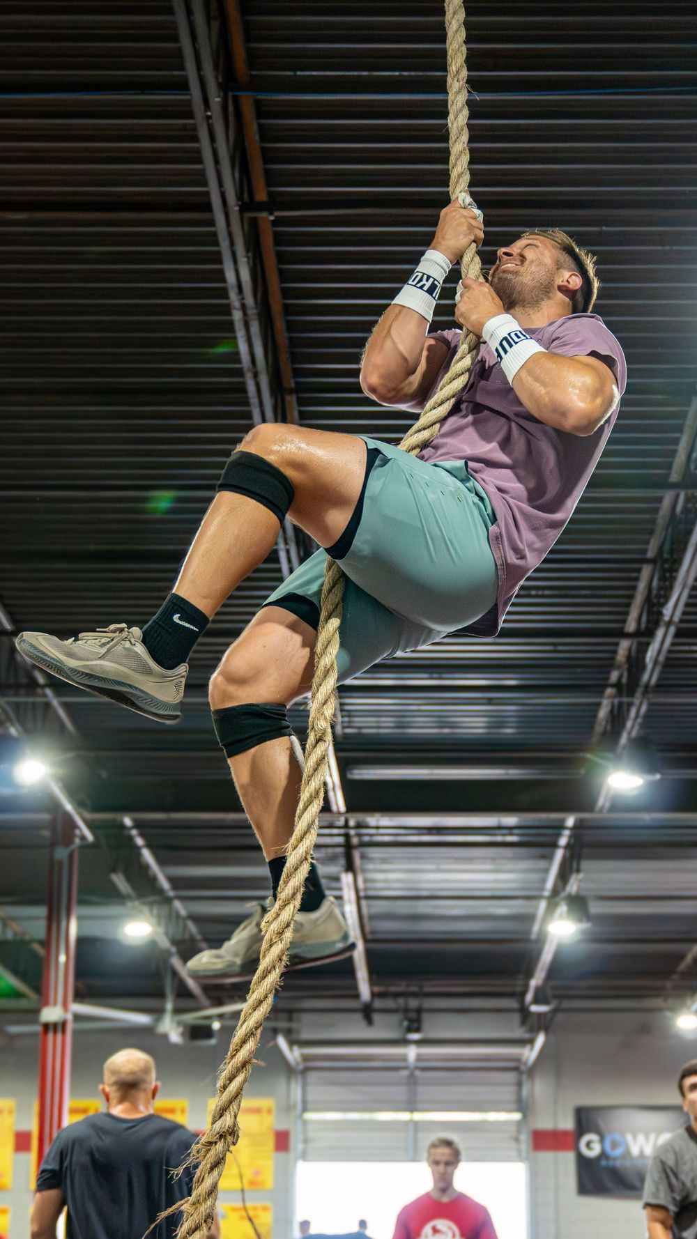 Athletes demonstrate progressive rope climbing technique in an indoor fitness facility.