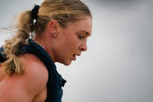 Close-up profile of blonde female athlete with ponytail sweating during outdoor sports competition.