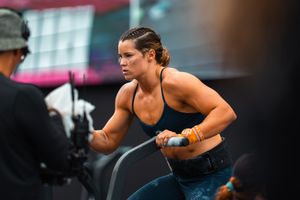 Woman intensely working out on an air bike machine during a CrossFit competition, wearing a blue sports top.