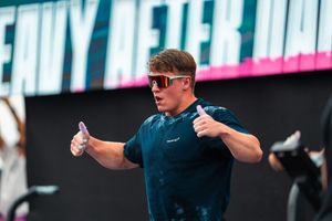Fit male athlete wearing red sunglasses giving thumbs up at fitness competition event.