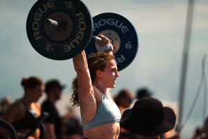 Female CrossFit athlete lifting Rogue barbell overhead during outdoor weightlifting competition.