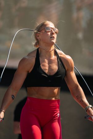 Muscular female athlete jump roping outdoors in red leggings and black sports bra during a fitness competition.