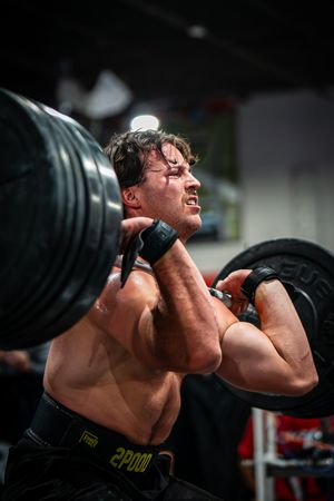 Muscular athlete performing a front squat with heavy barbell in dark gym setting.