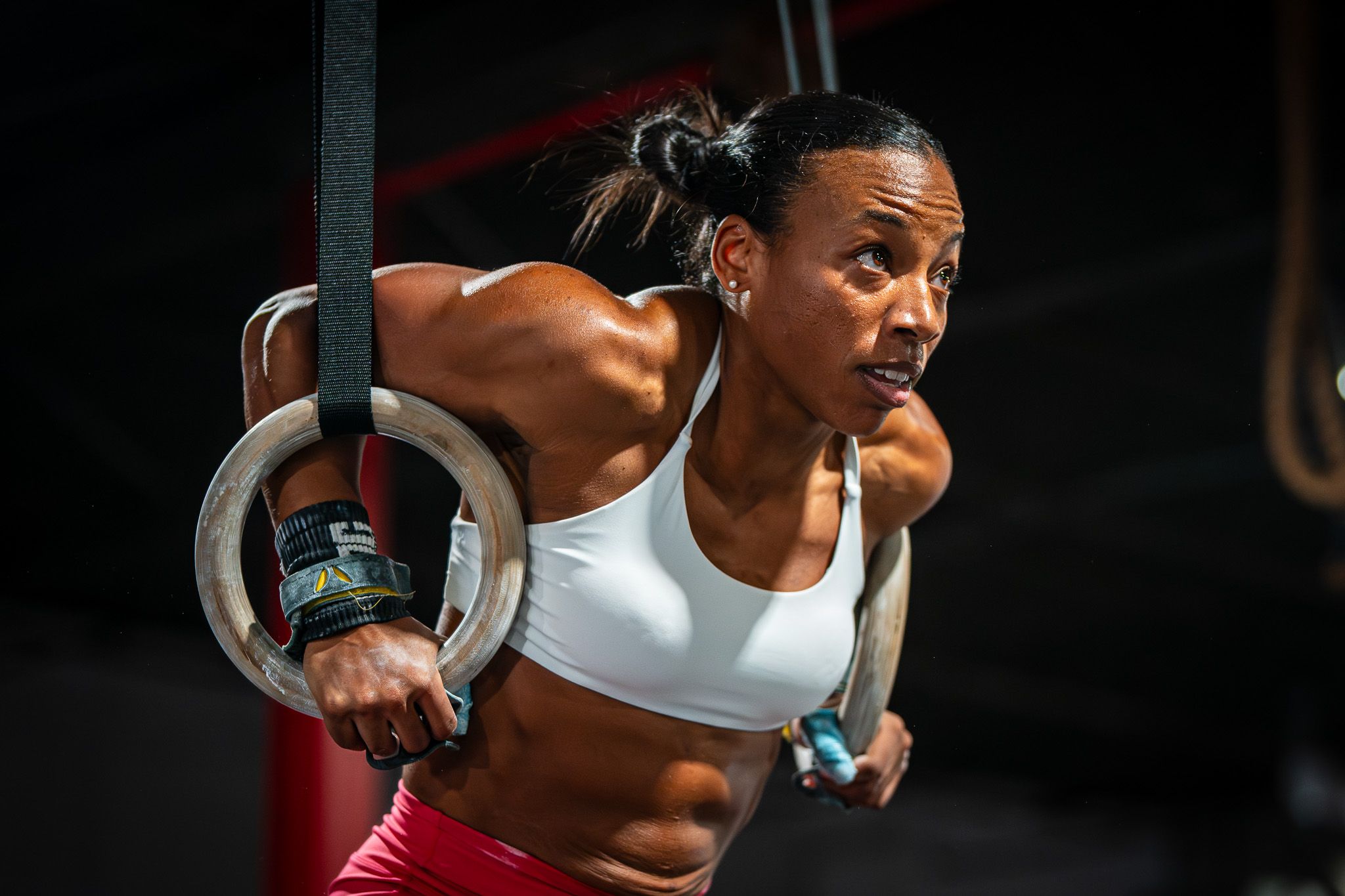 Athletic person performing exercises on gymnastic rings in dimly lit gym.