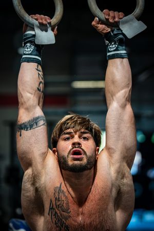 Muscular athlete performing intense ring muscle up exercise in gym.