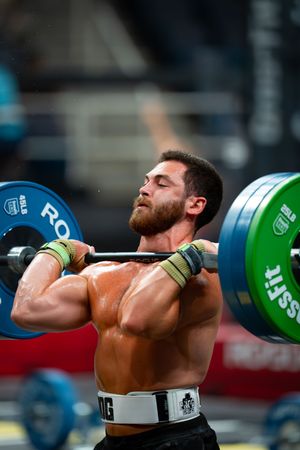 Athlete performing a heavy clean and jerk lift with green weight plates during CrossFit competition.